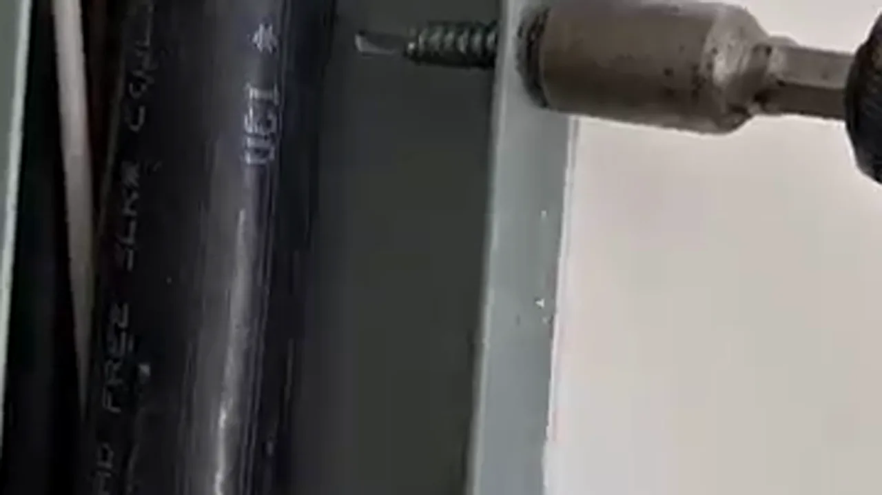 Close-up of a pointed wood screw threading into the side of a residential breaker panel near live conductors